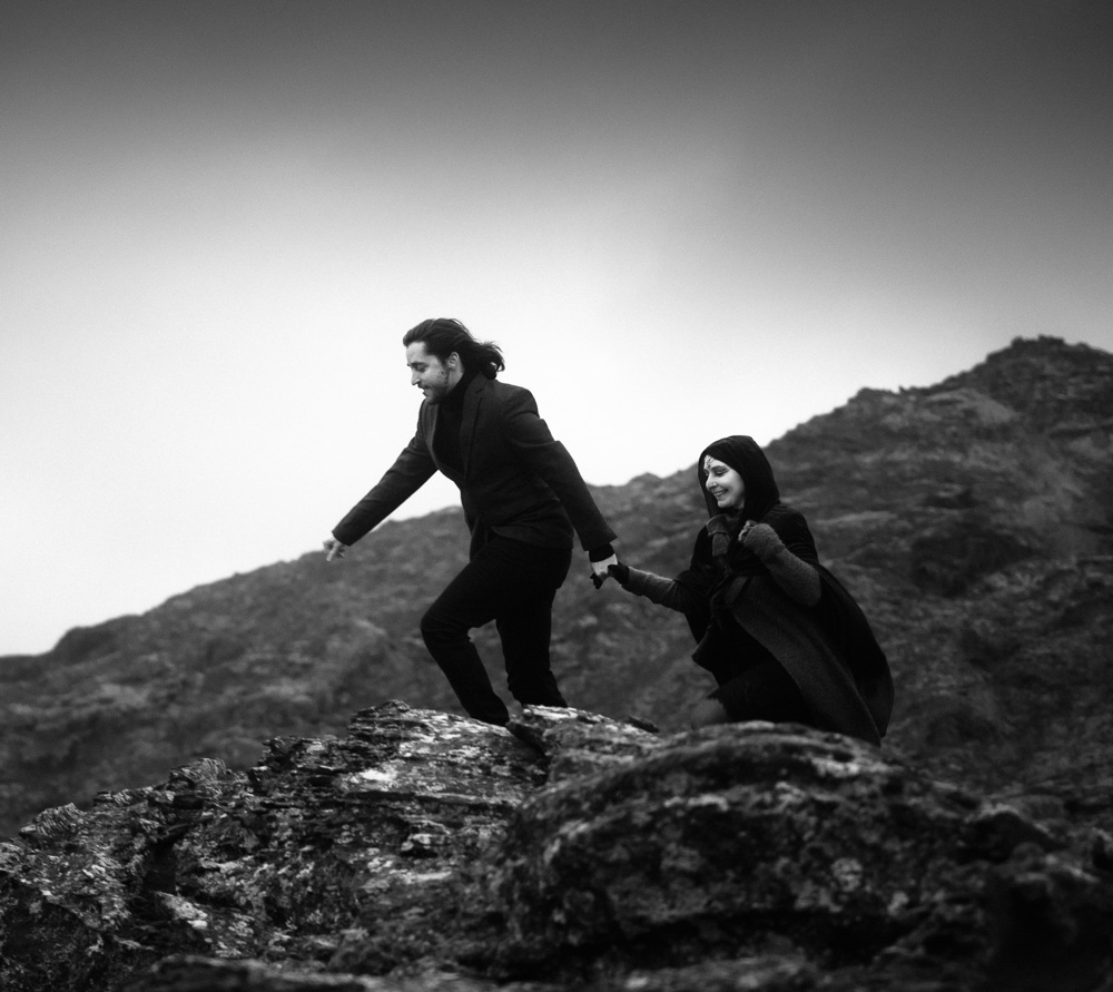 A young man holding a smiling woman's hand and climbing on a rock during their elopement in Iceland.